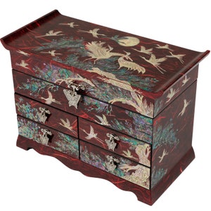 May include: A red wooden jewelry box with intricate inlaid designs of cranes and pine trees. The box has five drawers with silver butterfly-shaped handles.