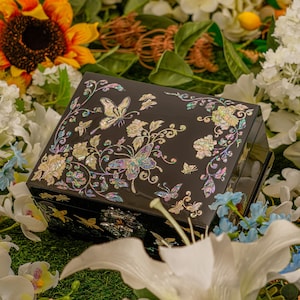 May include: A black wooden jewelry box with a floral and butterfly design inlaid with mother of pearl. The box has a hinged lid and a decorative metal clasp.