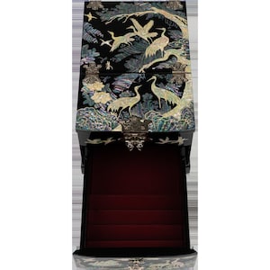 An elaborate black jewelry box with a red interior and oriental bird designs on the outside, isolated on a background.