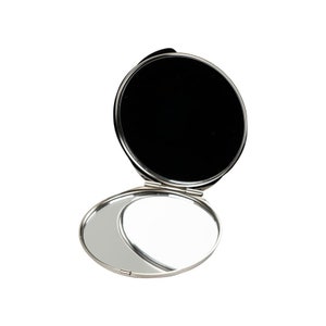 A simple, round compact mirror is open, showing one regular mirror and a blank, black space where a second mirror could be, against a white background.