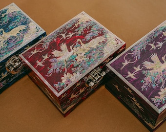 May include: Three decorative wooden boxes with intricate designs featuring cranes and flowers. The boxes are painted in shades of blue, red, and purple, and have a mother-of-pearl inlay.