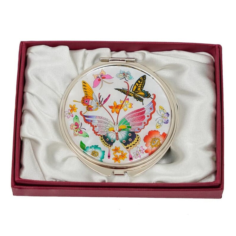 This is a compact mirror with a white background and an illustration of colorful butterflies and flowers. It is presented in a red box lined with white satin fabric