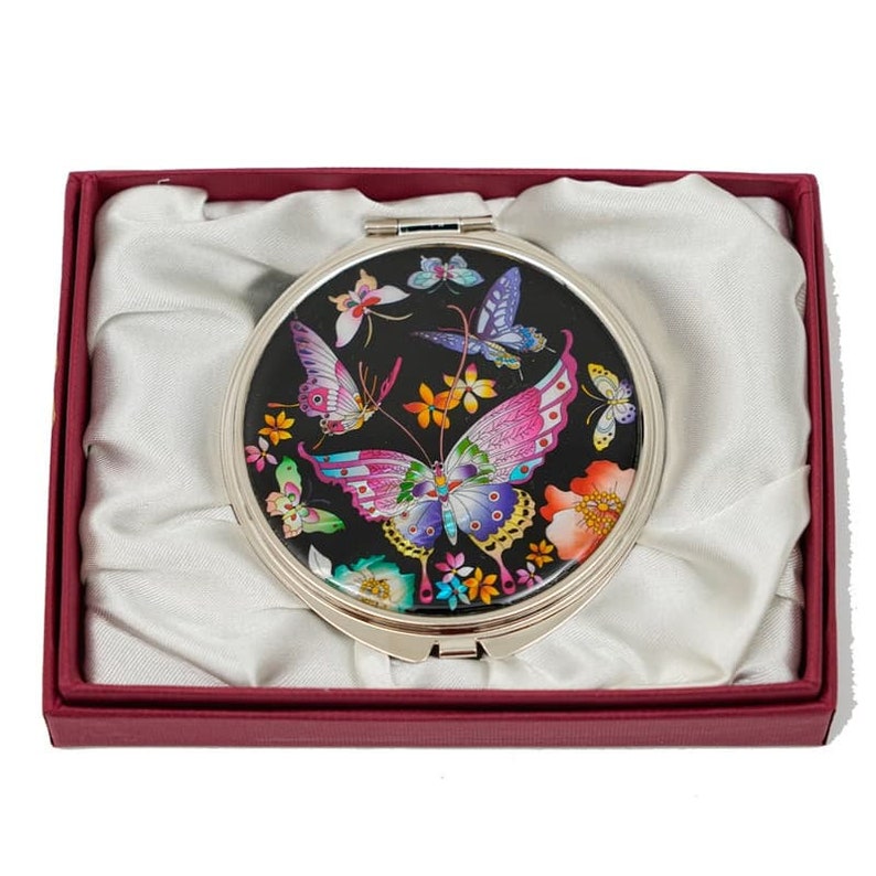 A vibrant compact mirror featuring various colorful butterflies and flowers on a black background, housed in a red gift box with a white satin interior
