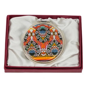 A round compact mirror featuring a vibrant, multicolored, paisley and floral pattern, presented in a burgundy box with a satin interior