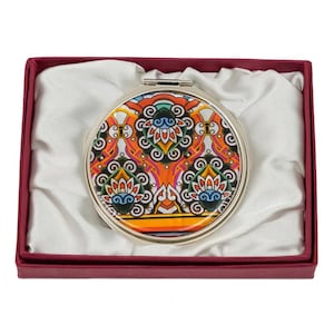 A round compact mirror featuring a vibrant, multicolored, paisley and floral pattern, presented in a burgundy box with a satin interior