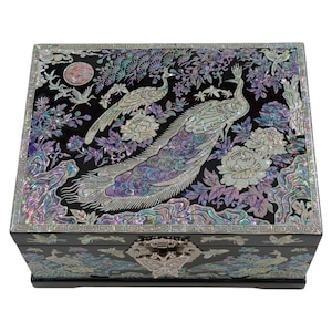 Peut inclure: Coffret à bijoux noir avec incrustation irisée de paons et de fleurs. La boîte est de forme rectangulaire avec un fermoir argenté. Le couvercle est orné de deux paons, de fleurs et de feuillage. Un objet de rangement décoratif.