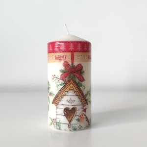 May include: White pillar candle with a Christmas design featuring a birdhouse, a red bow, and the text "Merry Christmas".