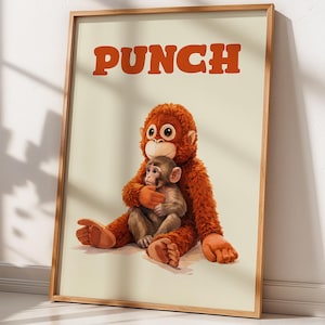 May include: A framed print featuring a whimsical illustration of a large, orange, plush orangutan hugging a smaller monkey. The word "PUNCH" is printed in orange block letters at the top. The artwork is set against a cream-colored background.