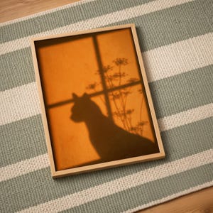 Cat shadow poster featuring a minimalist orange silhouette of a cat sitting by a sunlit window, with soft plant shadows on a textured amber wall. Moody aesthetic wall art perfect for bedrooms, reading nooks, or hallways. Warm sunset-toned cat silhouette print, a unique gift for cat lovers who enjoy dreamy, atmospheric wall decor rather than literal pet portraits.