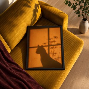 Cat shadow poster featuring a minimalist orange silhouette of a cat sitting by a sunlit window, with soft plant shadows on a textured amber wall. Moody aesthetic wall art perfect for bedrooms, reading nooks, or hallways. Warm sunset-toned cat silhouette print, a unique gift for cat lovers who enjoy dreamy, atmospheric wall decor rather than literal pet portraits.