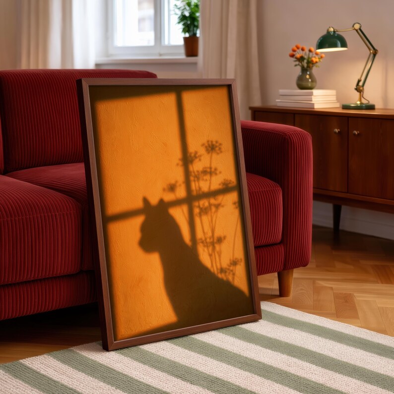 Cat shadow poster featuring a minimalist orange silhouette of a cat sitting by a sunlit window, with soft plant shadows on a textured amber wall. Moody aesthetic wall art perfect for bedrooms, reading nooks, or hallways. Warm sunset-toned cat silhouette print, a unique gift for cat lovers who enjoy dreamy, atmospheric wall decor rather than literal pet portraits.