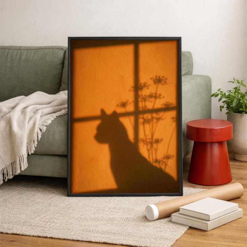 Cat shadow poster featuring a minimalist orange silhouette of a cat sitting by a sunlit window, with soft plant shadows on a textured amber wall. Moody aesthetic wall art perfect for bedrooms, reading nooks, or hallways. Warm sunset-toned cat silhouette print, a unique gift for cat lovers who enjoy dreamy, atmospheric wall decor rather than literal pet portraits.
