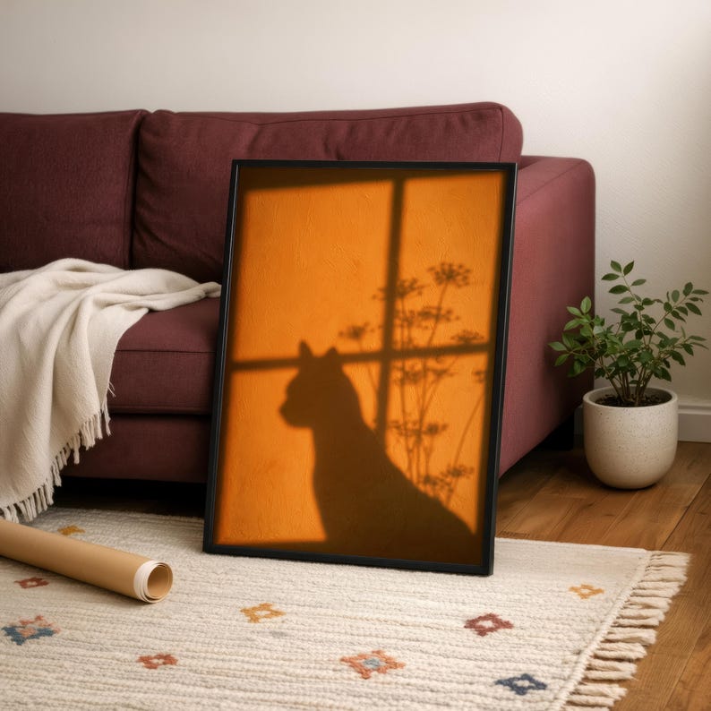 Cat shadow poster featuring a minimalist orange silhouette of a cat sitting by a sunlit window, with soft plant shadows on a textured amber wall. Moody aesthetic wall art perfect for bedrooms, reading nooks, or hallways. Warm sunset-toned cat silhouette print, a unique gift for cat lovers who enjoy dreamy, atmospheric wall decor rather than literal pet portraits.