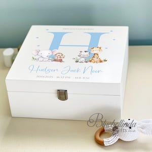 May include: A white wooden keepsake box with a light blue "H" and the words "Precious Memories" at the top. The box is decorated with cartoon animals and the name "Hudson Jack Noor" in light blue. The box measures 2.8 kg.