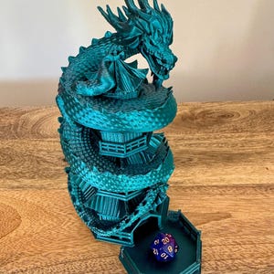 May include: A teal green 3D printed dragon tower dice rolling tower with a blue and gold dice inside. The tower is shaped like a dragon coiled around a tower with multiple levels.
