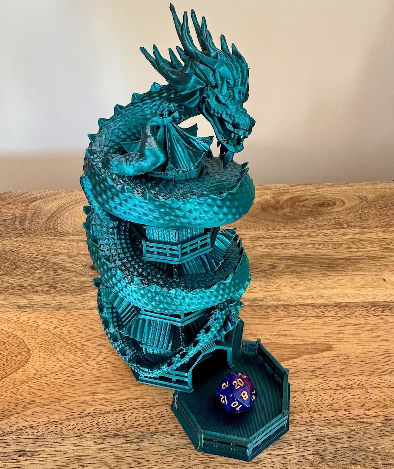 May include: A teal green 3D printed dragon tower dice rolling tower with a blue and gold dice inside. The tower is shaped like a dragon coiled around a tower with multiple levels.