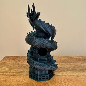 May include: A black 3D printed dragon statue wrapped around a tower. The dragon is curled up with its head facing upwards. The tower has a round opening in the center.