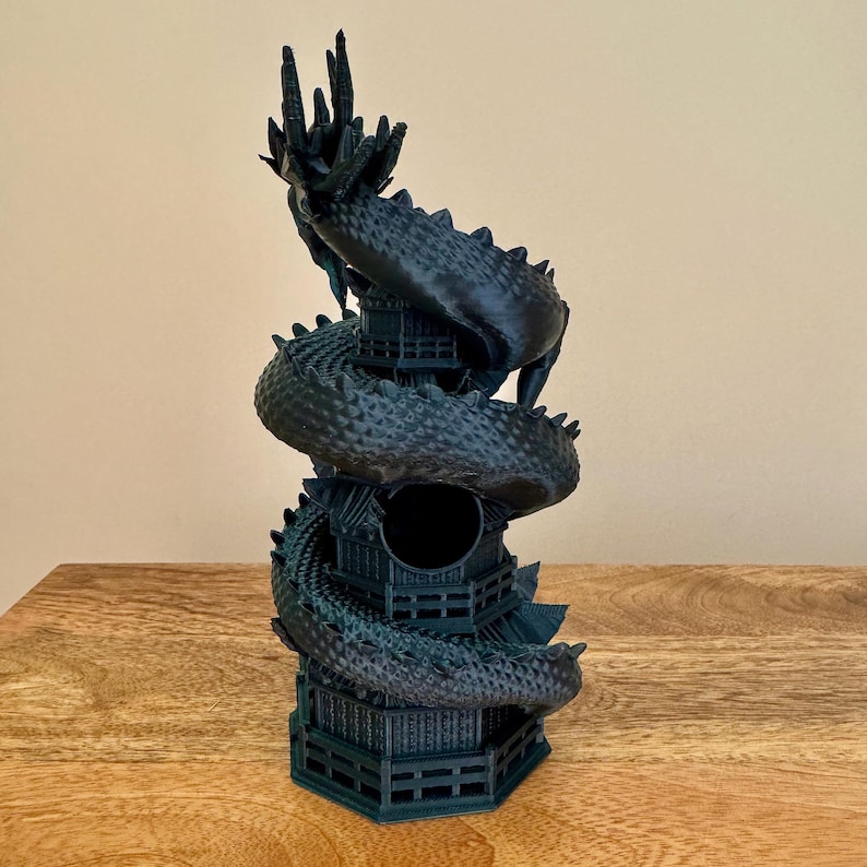 May include: A black 3D printed dragon statue wrapped around a tower. The dragon is curled up with its head facing upwards. The tower has a round opening in the center.