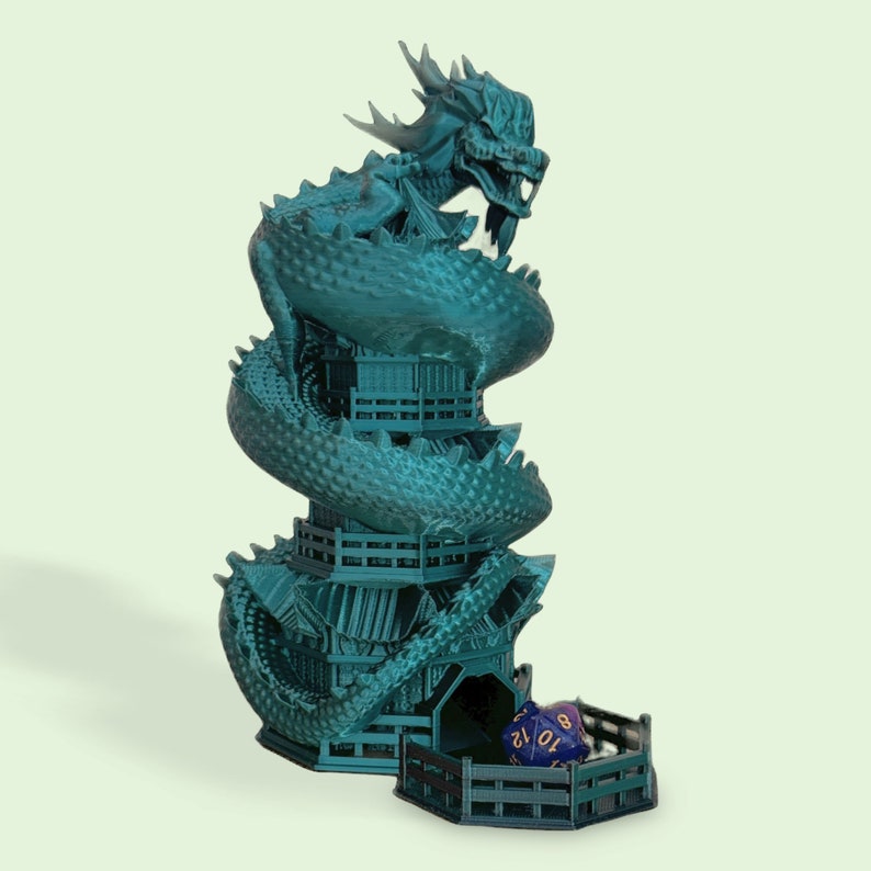 May include: A teal blue dragon-shaped dice tower with a multi-level design. The tower has a small opening at the bottom for dice to roll out. Two blue dice with gold numbers are in the tower's base.