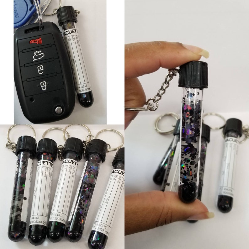 Op de afbeelding: Vijf zwarte en zilveren glitter gevulde reageerbuis sleutelhangers met zwarte dopjes en zilveren kettingen. De reageerbuizen hebben labels met de tekst "ACUET" en nummers.
