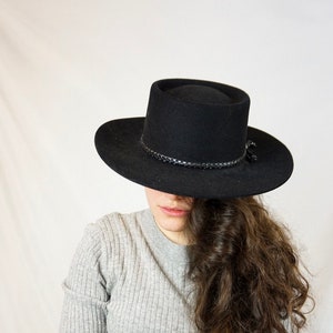 May include: A person wearing a black fedora hat and a gray sweater.