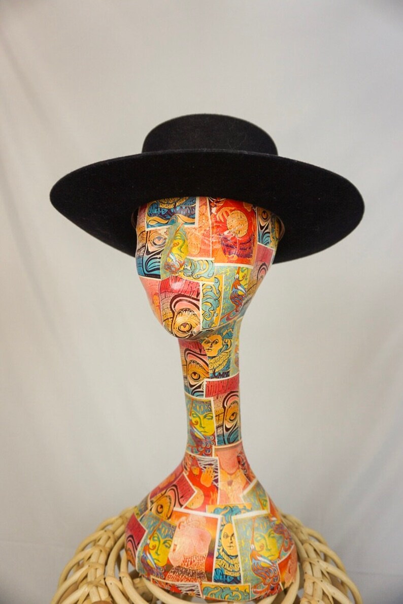 Puede incluir: Un sombrero fedora de fieltro negro con un ala ancha y una copa plana. El sombrero est&aacute; colocado sobre una cabeza de maniqu&iacute; con un dise&ntilde;o estampado de colores.