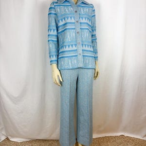 May include: A light blue two-piece knit suit. The button-down shirt features a geometric pattern in shades of blue and white. The matching pants are wide-legged. The suit is displayed on a mannequin.