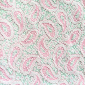 May include: White fabric with a pink and green paisley pattern.