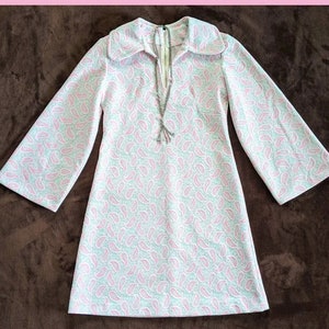 May include: A white and pink paisley patterned dress with a long collar and long sleeves. The dress has a V-neckline and a silver chain necklace.