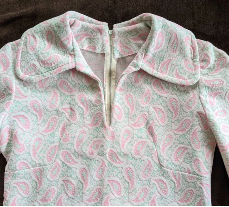 May include: A pink and green paisley patterned dress with a long zipper down the front.