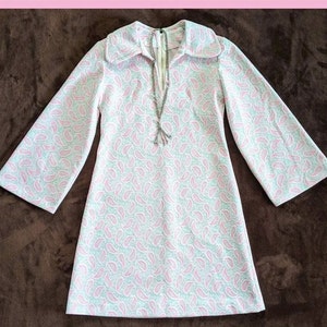 May include: A white and pink paisley print mini dress with a long, wide-sleeved design and a V-neckline. The dress has a collar and a zipper closure in the back.