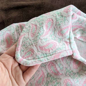 May include: Close-up of a pink and green patterned fabric with a white background. The fabric has a scalloped edge and is folded over.