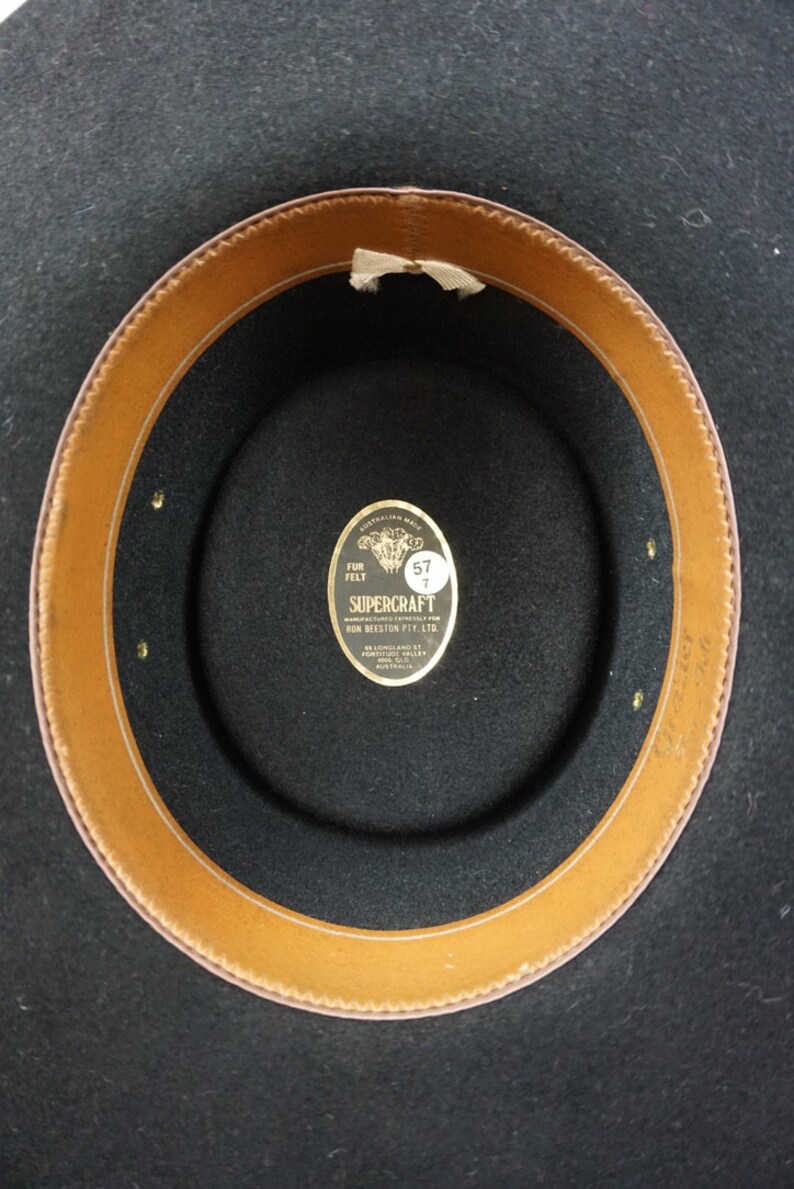 Puede incluir: El interior de un sombrero de fieltro negro con una banda de cuero marr&oacute;n. Una etiqueta dorada dice "SUPERCRAFT FUR FELT" con una etiqueta de tama&ntilde;o que dice "57 7".