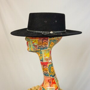Puede incluir: Un sombrero vaquero de fieltro negro con una banda de cuero trenzada y una hebilla plateada. El sombrero est&aacute; sentado en una cabeza de maniqu&iacute;.
