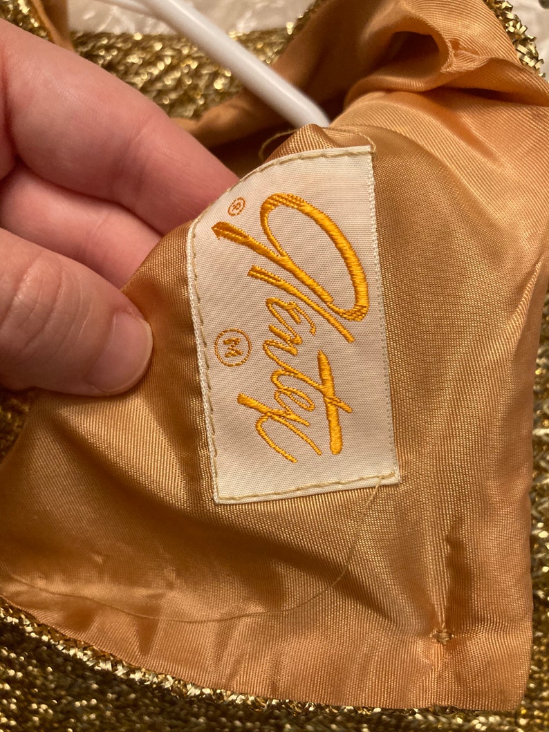 May include: A gold sequined dress with a white label that says "Oleg Cassini" and a size "M" tag.