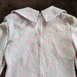 May include: A white dress with a pink and green paisley pattern. The dress has a zipper down the back and a large collar.