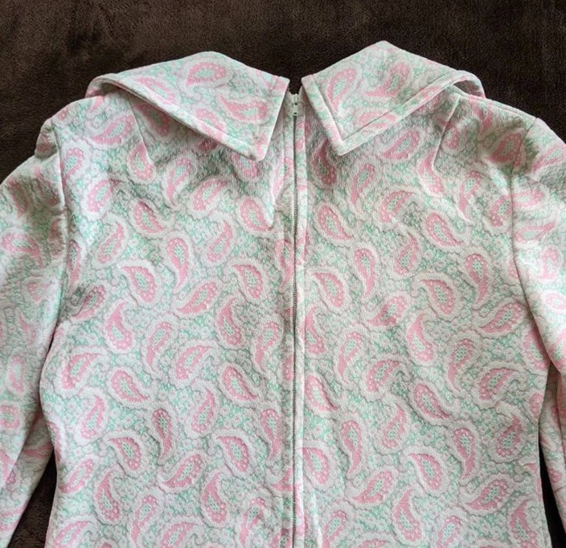 May include: A white dress with a pink and green paisley pattern. The dress has a zipper down the back and a large collar.