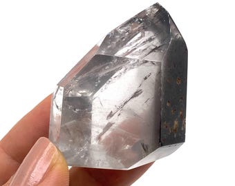 May include: A clear quartz crystal with a double terminated point and a black inclusion. The crystal is faceted and has a smooth, polished surface.