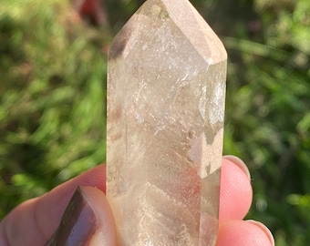 May include: A clear quartz crystal point with a light brown, cloudy, and translucent appearance. The crystal is approximately 2 inches tall and has a pointed tip.