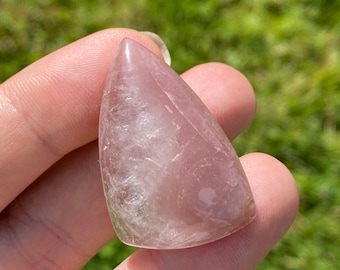 May include: A pale pink, triangular shaped, polished gemstone pendant with a white, cloudy, translucent appearance.