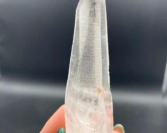 以下が含まれることがあります： 透明で尖った形状のクォーツクリスタルのタワー。半透明で多面的な構造をしており、内部には目に見えるインクルージョン、垂直な面に沿った自然な筋、そして小さなオレンジブラウンの鉱物の斑点が確認できます。