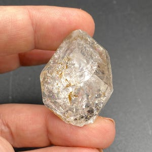 Pode incluir: Um cristal de quartzo transparente com uma ponta dupla, também conhecido como diamante Herkimer. O cristal tem uma superfície natural e áspera e mede aproximadamente 5 cm de comprimento.