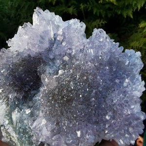 May include: A large amethyst crystal cluster with a purple and white color. The crystal has a rough, natural texture and is surrounded by smaller crystals.