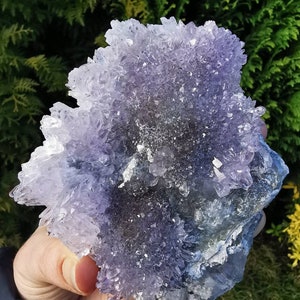 May include: A large amethyst crystal cluster with a purple and white color gradient. The crystal has a rough, natural texture and is surrounded by smaller crystals.
