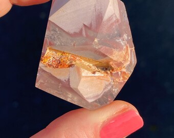 May include: A clear, faceted crystal with a pink and white pattern and a thin band of orange and brown running through the center.