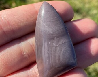 May include: A polished, gray, and white, pointed, gemstone with swirling patterns.