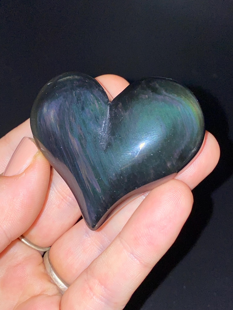 Puede incluir: Un cristal de obsidiana en forma de coraz&oacute;n con colores arco&iacute;ris iridiscentes. El cristal est&aacute; pulido y liso.