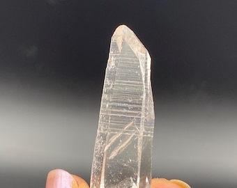 May include: A clear quartz crystal with striations, a type of mineral commonly used in jewelry and healing practices.