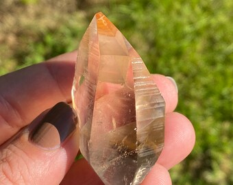 May include: A clear quartz crystal point with a double termination. The crystal has a light orange hue and is approximately 2 inches in length.