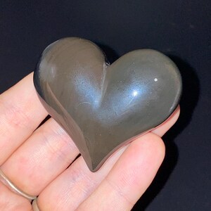 Puede incluir: Una piedra de obsidiana en forma de coraz&oacute;n de color gris oscuro con un ligero brillo iridiscente.